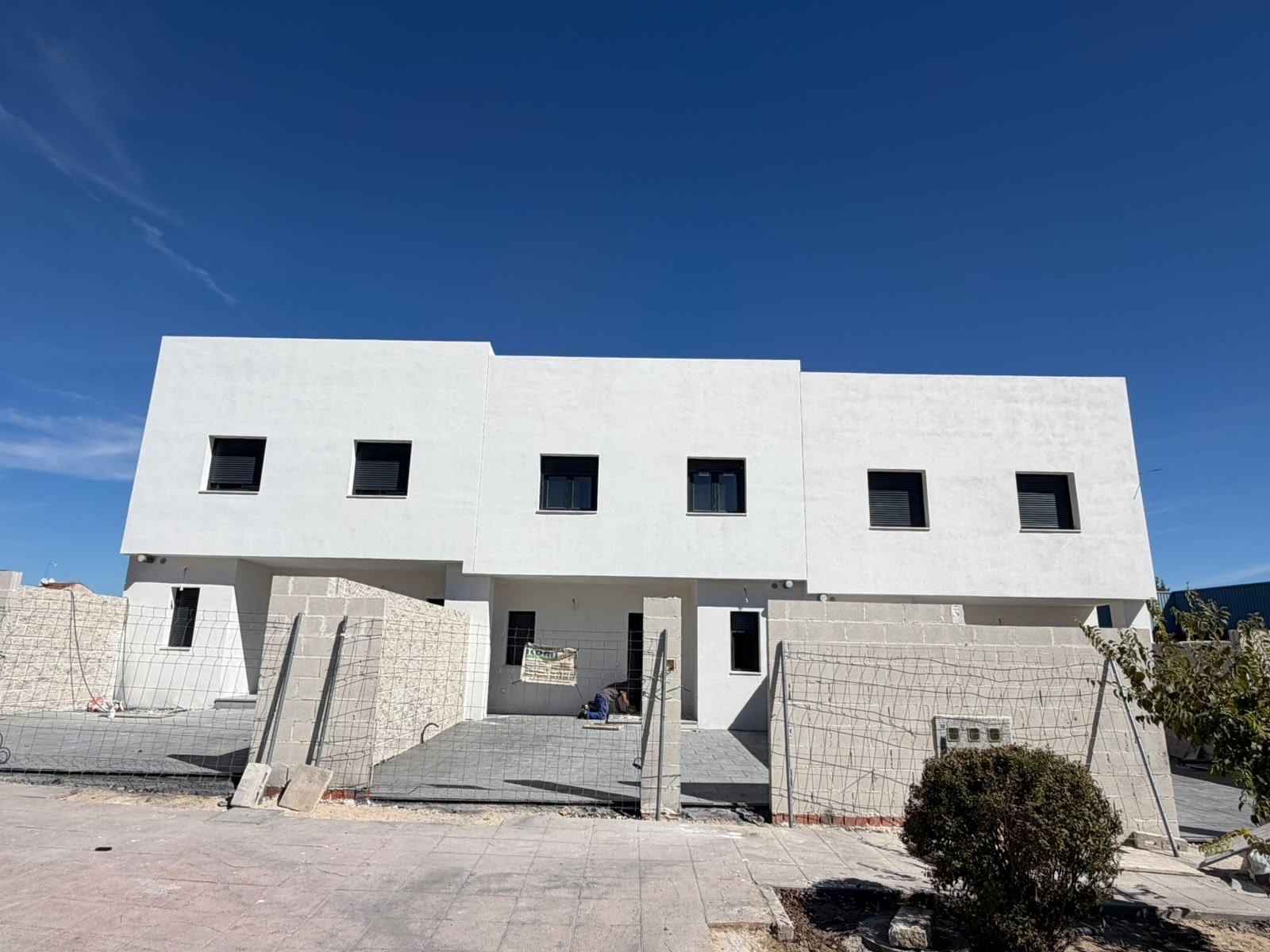 Vivienda unifamiliar de obra nueva de GRAMA HOMES con fachada blanca, carpintería en negro y porche de aparcamiento bajo cielo azul